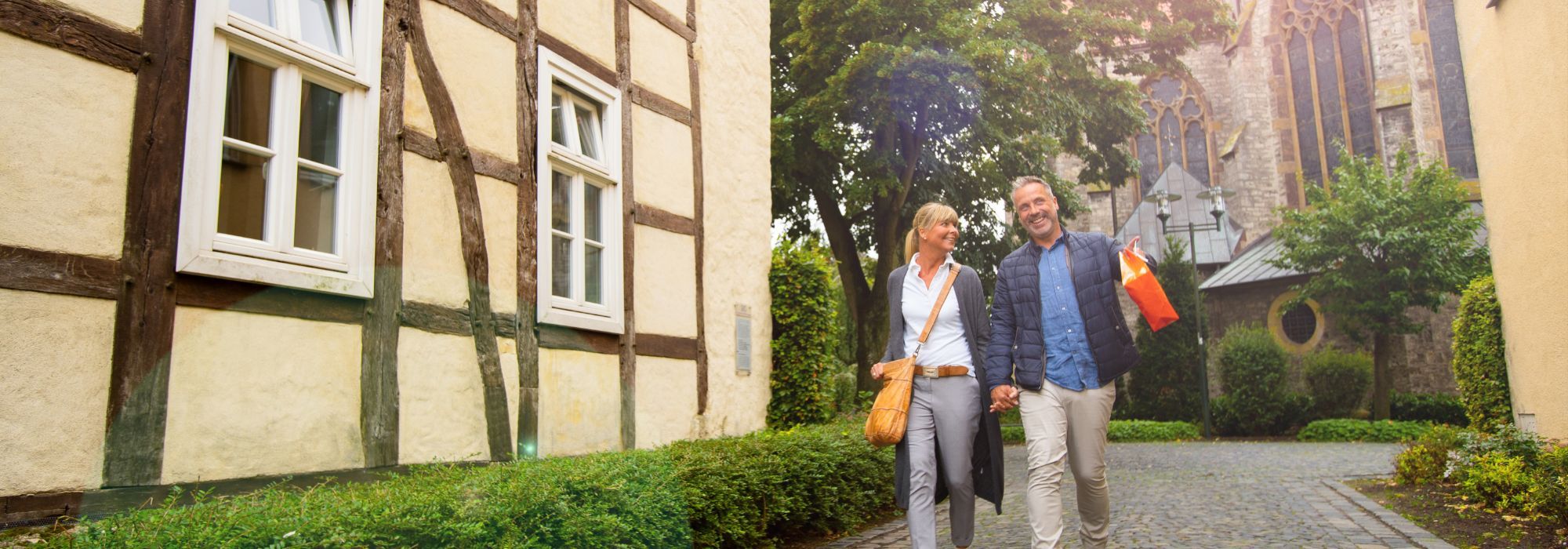 Eine Frau und ein Mann gehen mit Einkaufstüten an einem Fachwerkhaus vorbei