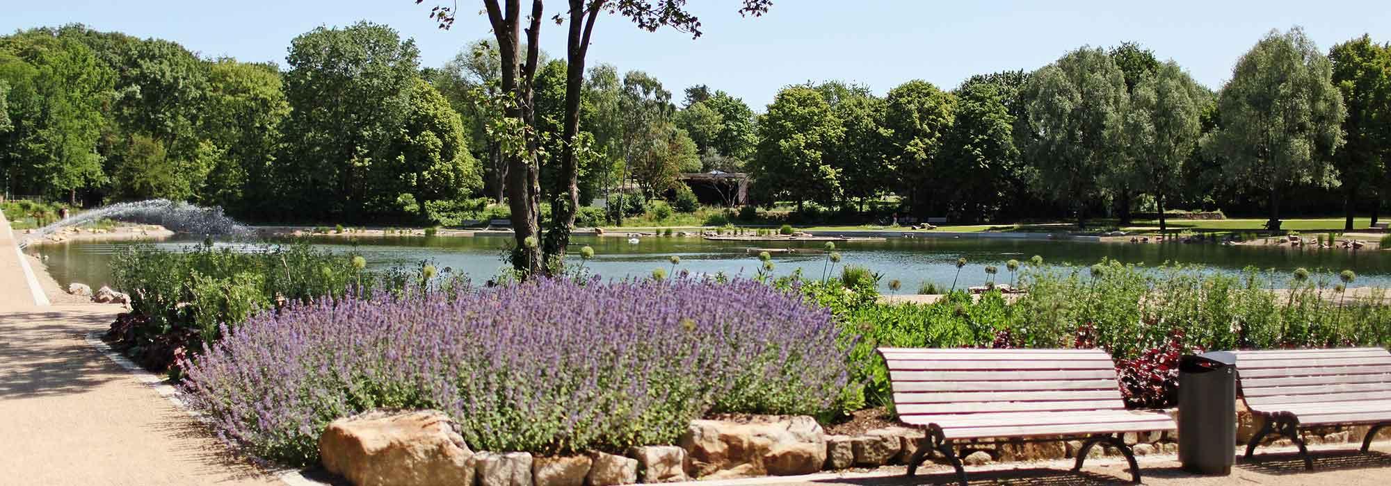 Kurpark mit Bänken, Grünflächen und Gewässer bei blauem Himmel