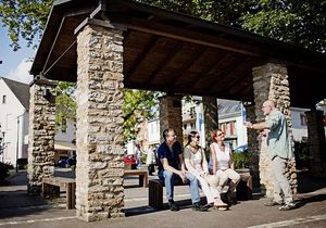 Ein Mann und zwei Frauen sitzen auf einer Bank und bekommen etwas von einem anderen Mann erklärt