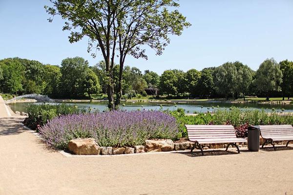 Kurpark mit Bänken, Grünflächen und Gewässer bei blauem Himmel