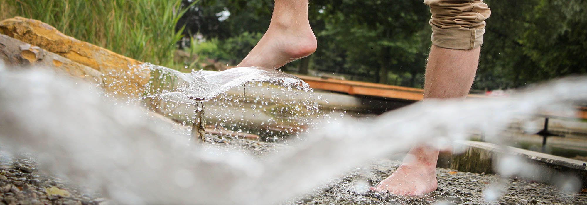 Mensch hält seine Füße zur Abkühlung an das Wasserspiel