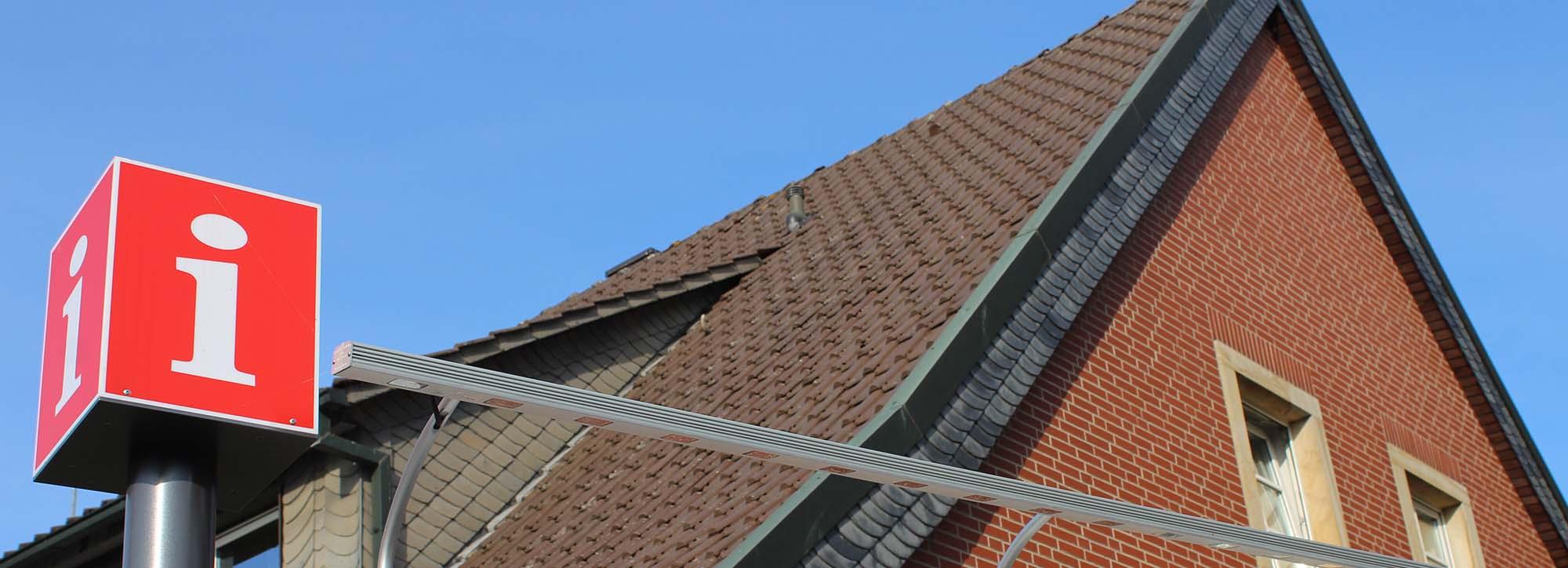 Rotes Informationsschild vor einem Haus und blauem Himmel