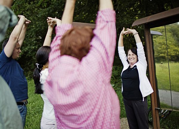 Eine kleine Menschengruppe macht einer Frau Fitnessübungen nach