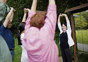 Eine kleine Menschengruppe macht einer Frau Fitnessübungen nach