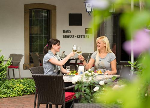 Zwei Frauen sitzen draußen und stoßen mit einem Glas Wein an