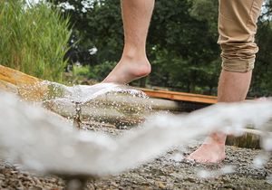 Mensch hält seine Füße zur Abkühlung an das Wasserspiel