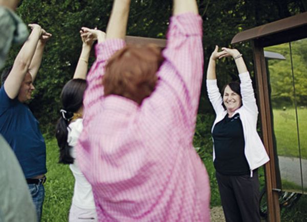 Eine kleine Menschengruppe macht einer Frau Fitnessübungen nach