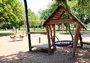 Ein kleines Haus, eine Nestschaukel und andere Spielgeräte auf einem Spielplatz