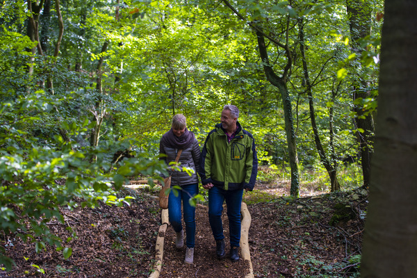 Pärchen läuft über einen mit Holzbohlen eingefassten Rindenmulch-Pfad im Wald.