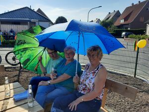 Drei Damen genießen das schöne Wetter unter zwei großen Regenschirmen als Sonnenschutz auf einer Bank auf dem neueröffneten Spielplatz am Heidering in Bad Laer.