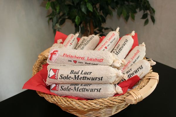 Im Korb liegen Würste.
Die Würste sind von der Fleischerei Lauhoff.
Die Würste heißen Sole-Mettwürste.
Der Korb steht auf einem Tisch.