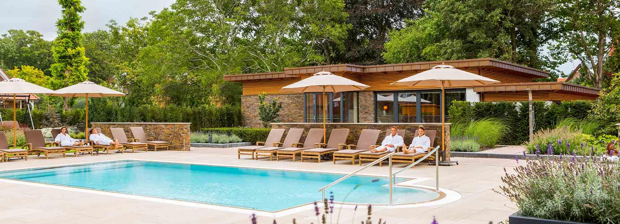 Ansicht eines Hotelpools draußen mit Sonnenschirmen im Grünen