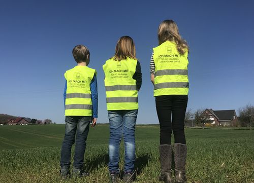 Foto von drei Kindern mit Rücken zur Kamera, die Warnwesten der Cleanup-Aktion tragen