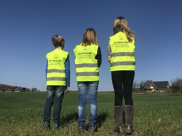 Foto von drei Kindern mit Rücken zur Kamera, die Warnwesten der Cleanup-Aktion tragen