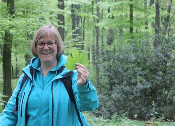 Eine Frau steht mit einem Blatt in der Hand im Wald