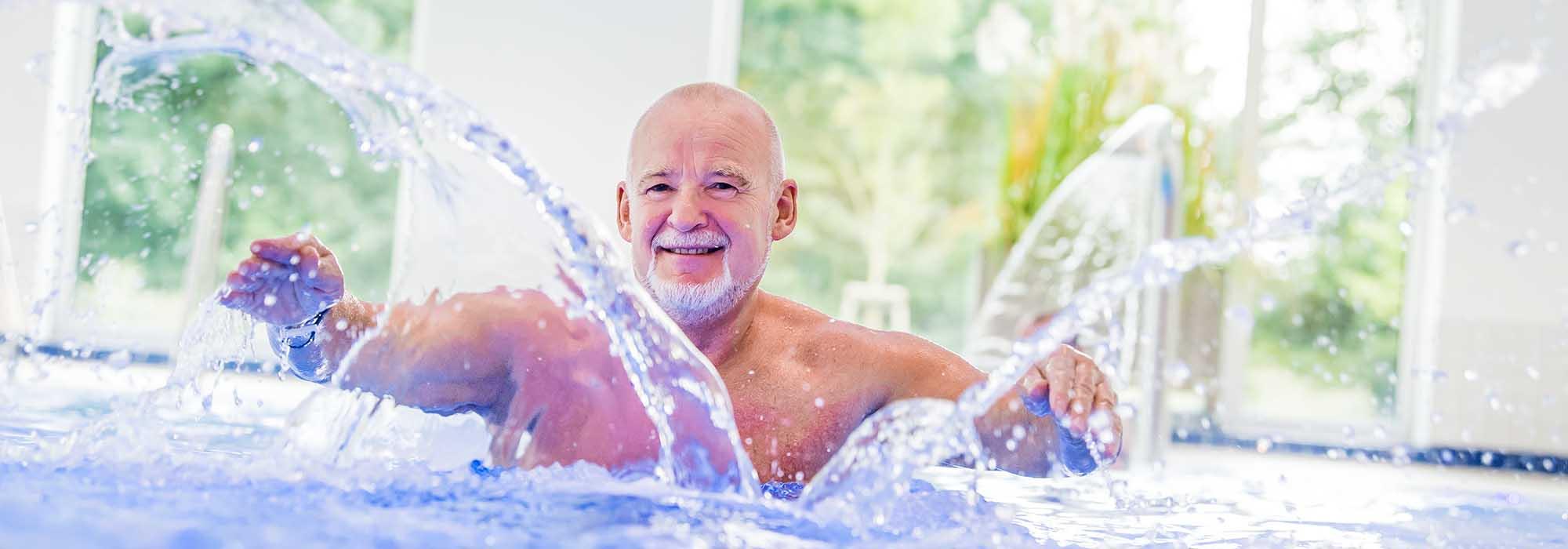 Ein Mann steht in einem Schwimmbecken und wirbelt Wasser mit den Händen auf