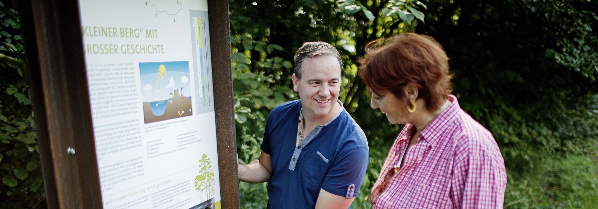 Ein Mann und eine Frau stehen vor einer Informationstafel im Grünen
