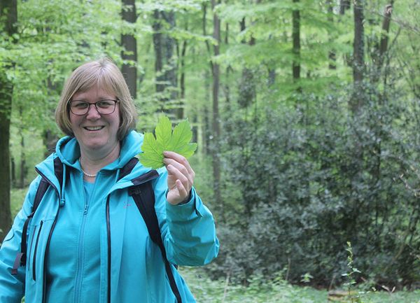 Eine Frau steht mit einem Blatt in der Hand im Wald
