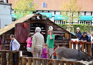 Eine Menschengruppe steht vor einer Holzhütte, vor der sich auch ein Esel befindet