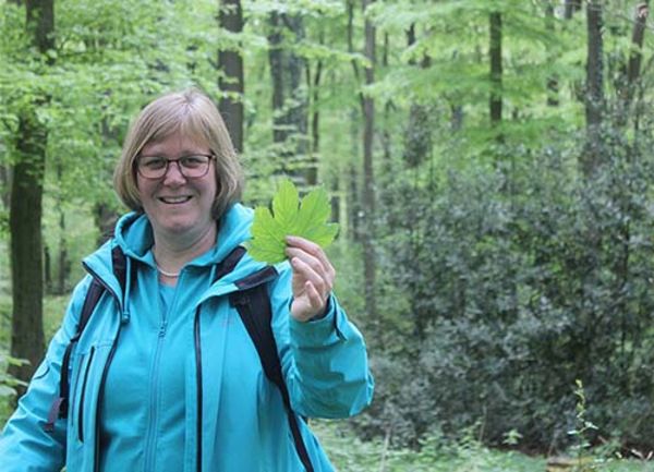 Eine Frau steht mit einem Blatt in der Hand im Wald