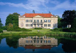 Großes Anwesen im Grünen mit Gewässer vor strahlend blauem Himmel